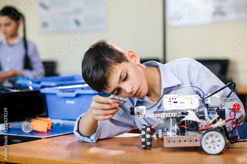 Little boy in robotics school makes robot managed from the constructor, child learns robot constructing.