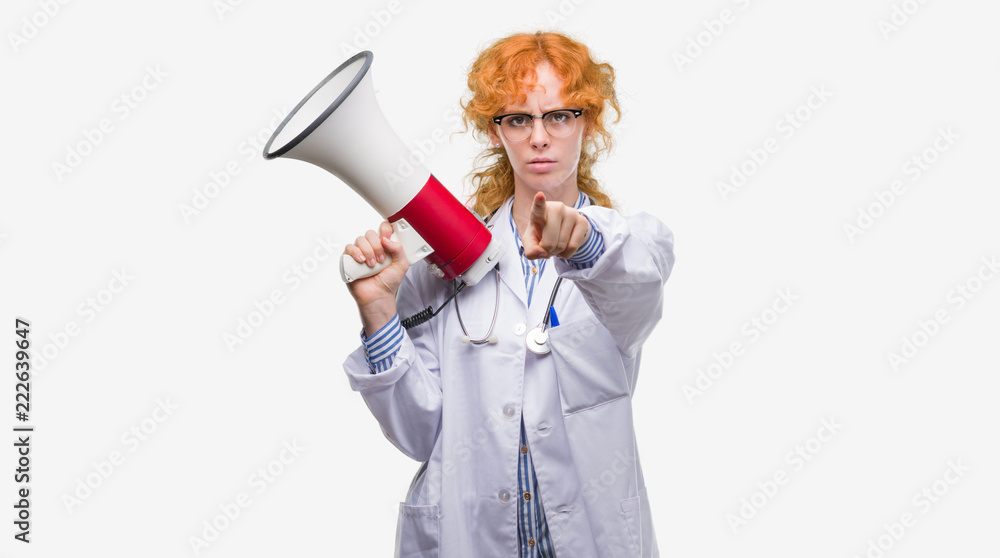 Young redhead doctor woman holding megaphone pointing with finger to the camera and to you, hand sign, positive and confident gesture from the front Young redhead doctor woman holding megaphone pointing with finger to the camera and to you, hand sign, positive and confident gesture from the front