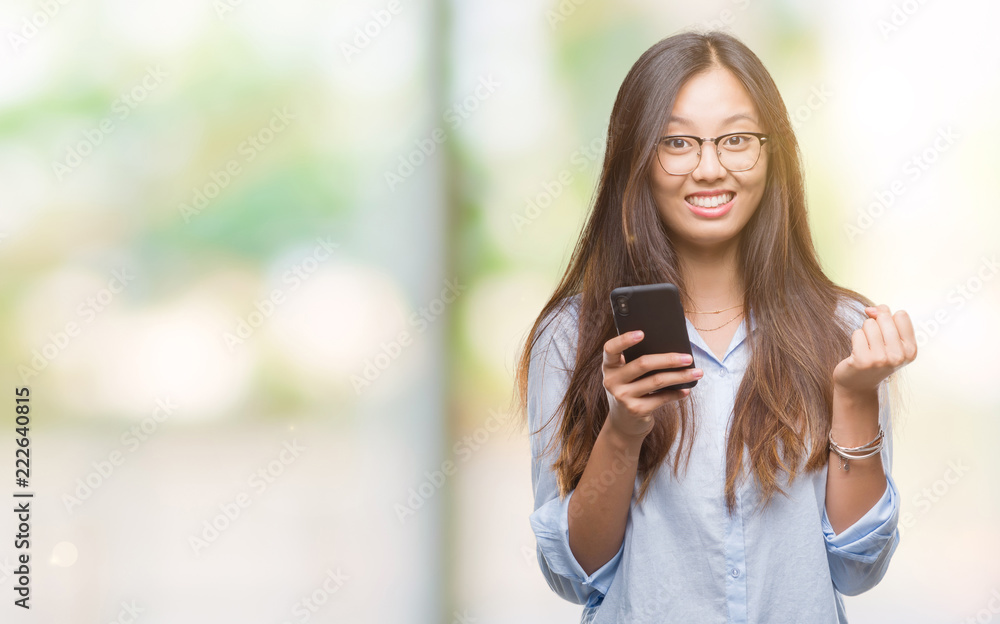 Young asian woman texting using smartphone over isolated background screaming proud and celebrating victory and success very excited, cheering emotion