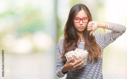Young asian woman eating popcorn over isolated background with angry face  negative sign showing dislike with thumbs down  rejection concept