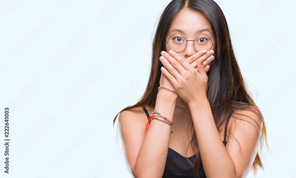 Young asian woman wearing glasses over isolated background shocked covering mouth with hands for mistake. Secret concept. Young asian woman wearing glasses over isolated background shocked covering mouth with hands for mistake. Secret concept.