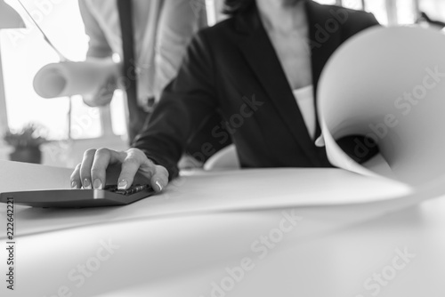 Bilde på lerret Greyscale image of businesswoman working on calculator as her partner stands beh