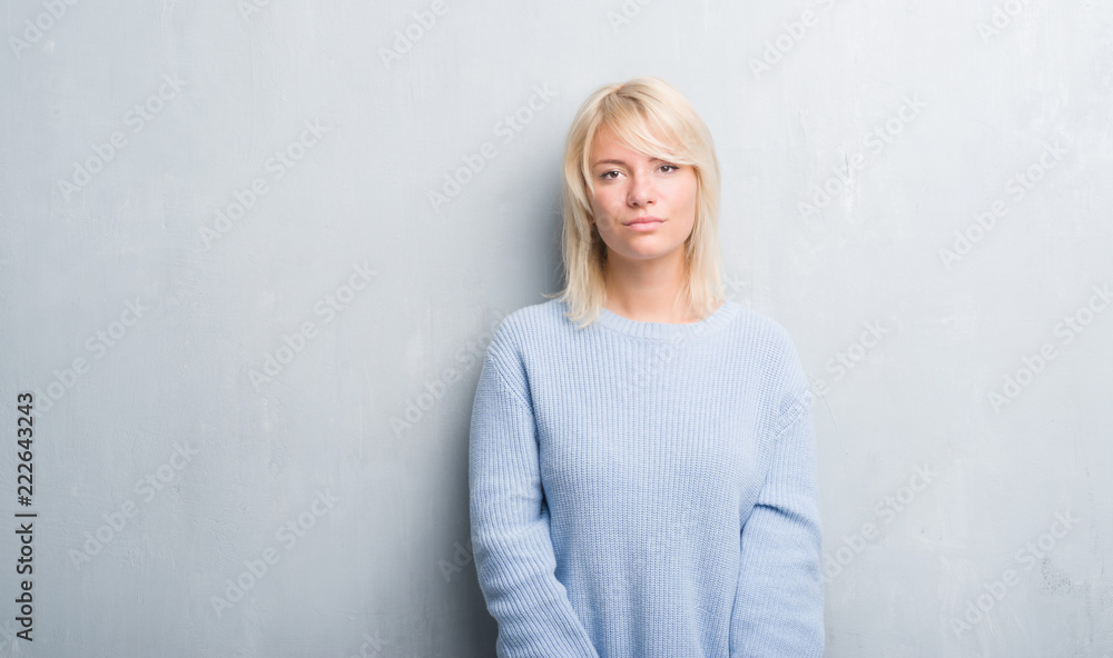 Adult caucasian woman over grunge grey wall wearing winter sweater with serious expression on face. Simple and natural looking at the camera. Adult caucasian woman over grunge grey wall wearing winter sweater with serious expression on face. Simple and natural looking at the camera.