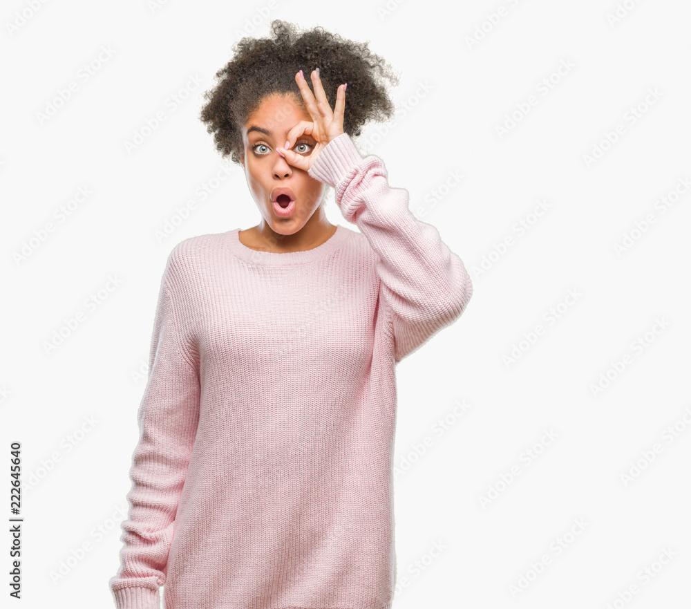 Young afro american woman wearing winter sweater over isolated background doing ok gesture shocked with surprised face, eye looking through fingers. Unbelieving expression. Young afro american woman wearing winter sweater over isolated background doing ok gesture shocked with surprised face, eye looking through fingers. Unbelieving expression.