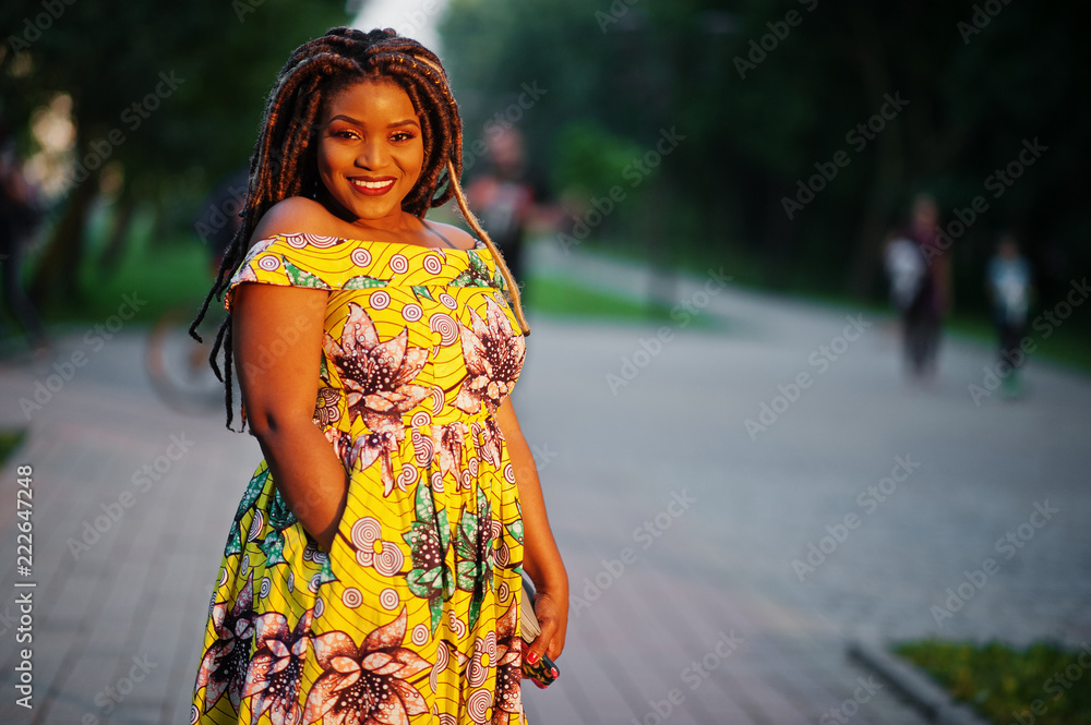 Cute small height african american girl with dreadlocks, wear at coloured yellow dress, posed at sunset.