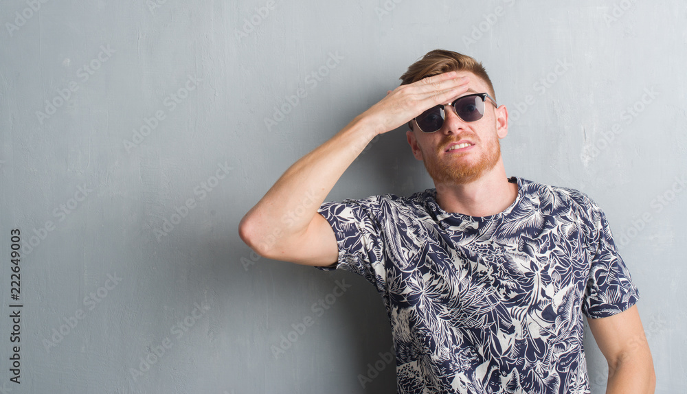 Young redhead man over grey grunge wall wearing sunglasses stressed with hand on head, shocked with shame and surprise face, angry and frustrated. Fear and upset for mistake. Young redhead man over grey grunge wall wearing sunglasses stressed with hand on head, shocked with shame and surprise face, angry and frustrated. Fear and upset for mistake.