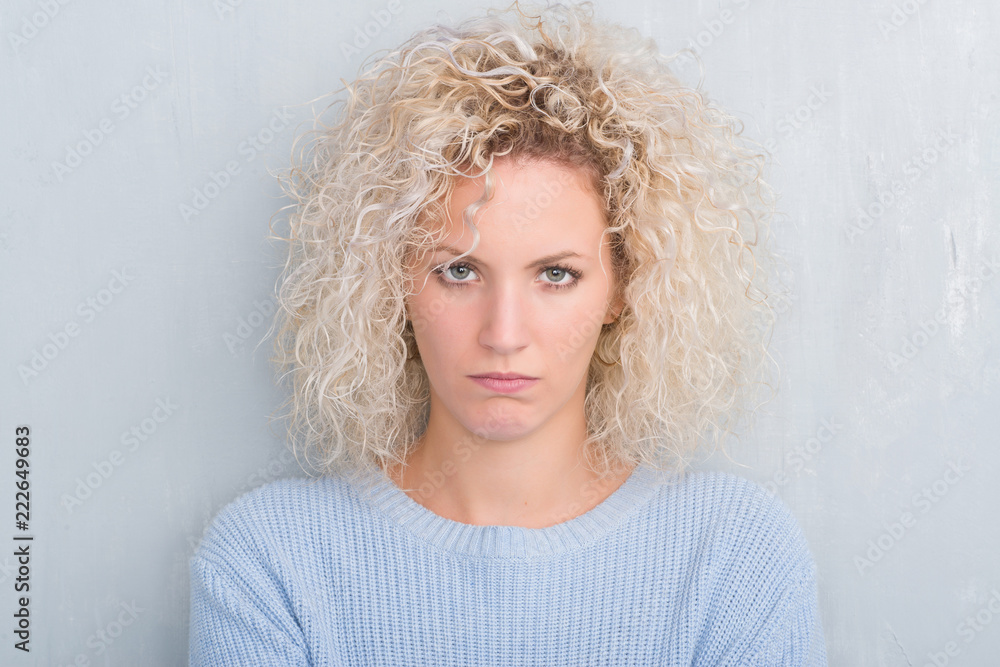 Young blonde woman with curly hair over grunge grey background skeptic and nervous, disapproving expression on face with crossed arms. Negative person. Young blonde woman with curly hair over grunge grey background skeptic and nervous, disapproving expression on face with crossed arms. Negative person.