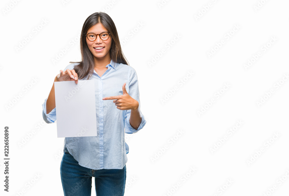 Young asian woman over isolated background holding blank paper very happy pointing with hand and finger Young asian woman over isolated background holding blank paper very happy pointing with hand and finger
