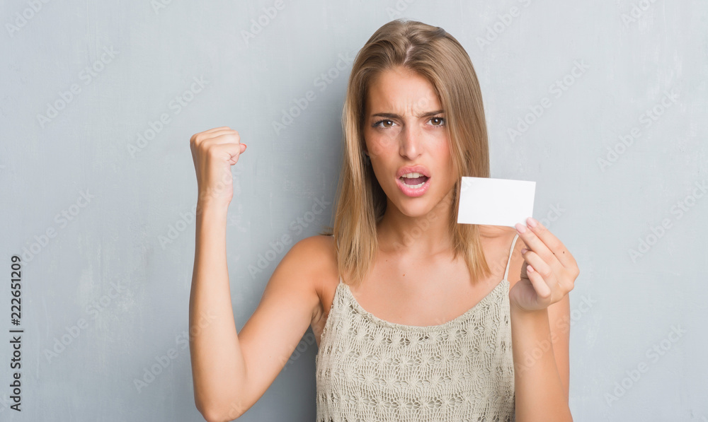 Beautiful young woman over grunge grey wall holding blank visit card annoyed and frustrated shouting with anger, crazy and yelling with raised hand, anger concept Beautiful young woman over grunge grey wall holding blank visit card annoyed and frustrated shouting with anger, crazy and yelling with raised hand, anger concept
