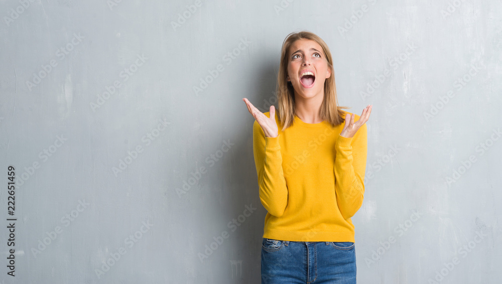 Beautiful young woman standing over grunge grey wall crazy and mad shouting and yelling with aggressive expression and arms raised. Frustration concept. Beautiful young woman standing over grunge grey wall crazy and mad shouting and yelling with aggressive expression and arms raised. Frustration concept.