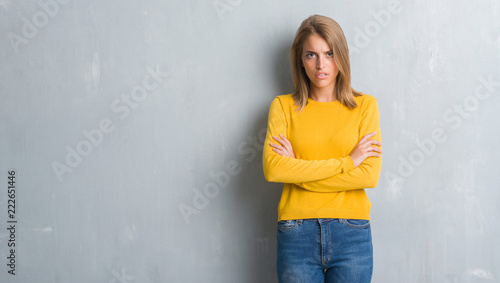 Beautiful young woman standing over grunge grey wall skeptic and nervous, disapproving expression on face with crossed arms. Negative person.