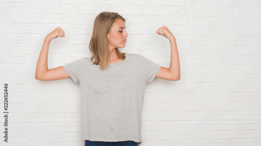 Beautiful young woman over white brick wall showing arms muscles smiling proud. Fitness concept. Beautiful young woman over white brick wall showing arms muscles smiling proud. Fitness concept.