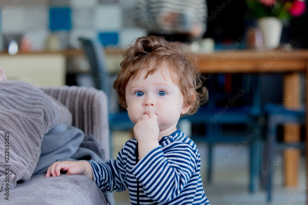 Little baby boy have a fun near a sofa on a house near a window. Looking at camera surprisingly Little baby boy have a fun near a sofa on a house near a window. Looking at camera surprisingly