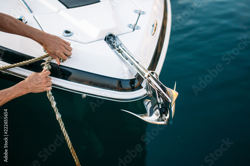 Man s hand with boat rope. Yachtsman moors his motor boat at jetty. Close up hands and bow of the boat. photo