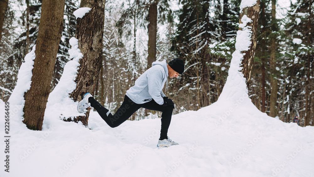 Runner doing stretching exercises in a snow forest 