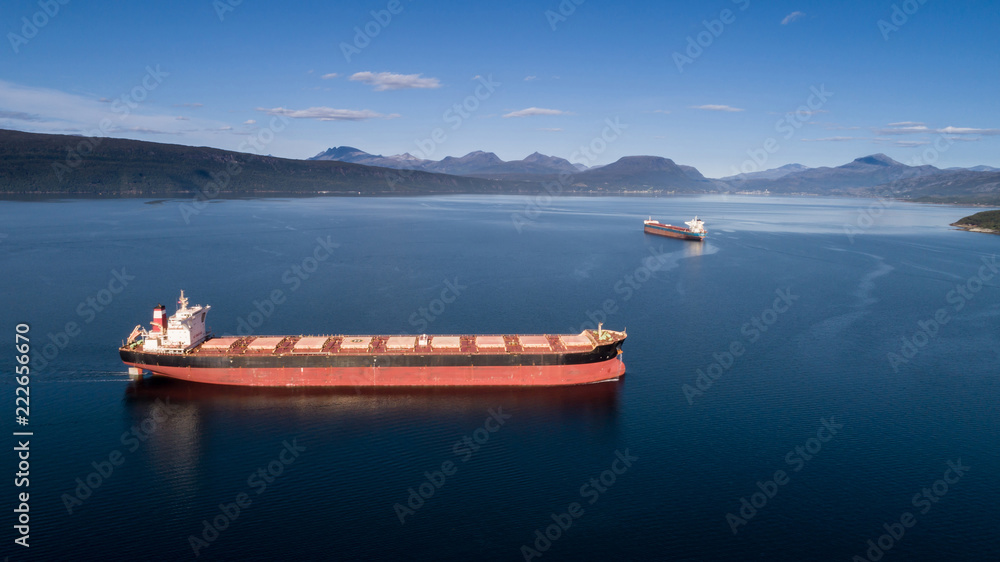 Aerial shot of a cargo ship on the open sea with other ship and mountains in the background, Narvik, Norway