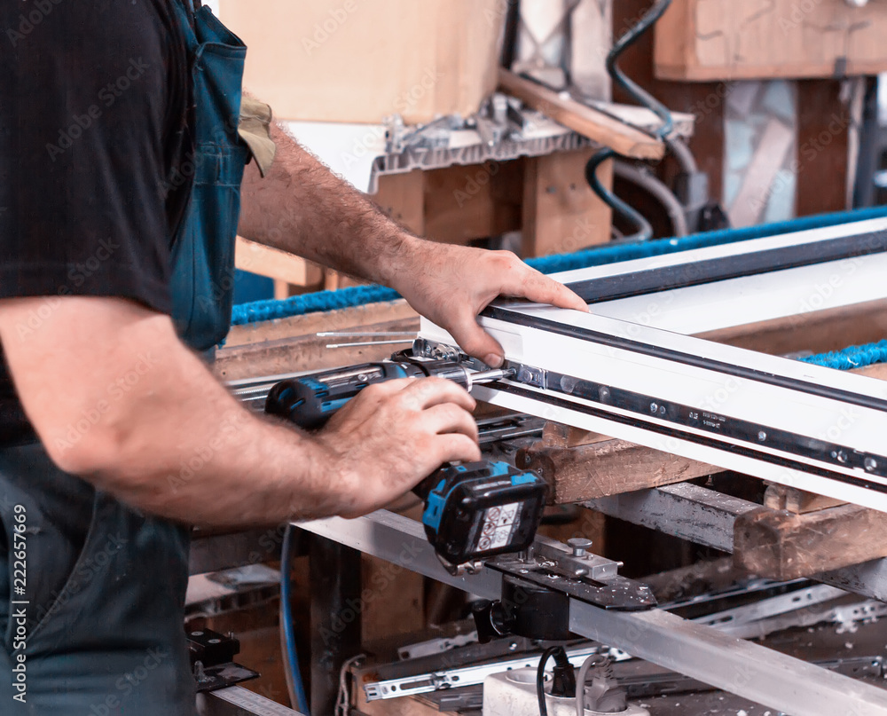 Production windows pvc, man screwed screwdriver hinged defense on the sash pvc frame, close-up, work Production windows pvc, man screwed screwdriver hinged defense on the sash pvc frame, close-up, work
