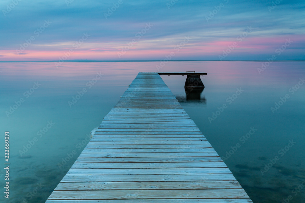 Jetty reaching out in the calm evening ocean at sunset.