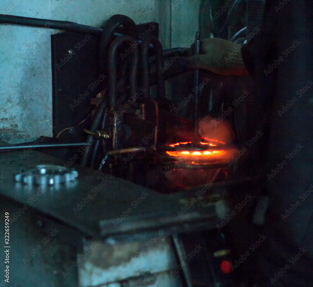 Φωτογραφία The worker makes hardening heat treatment of the metal gear on a special machine