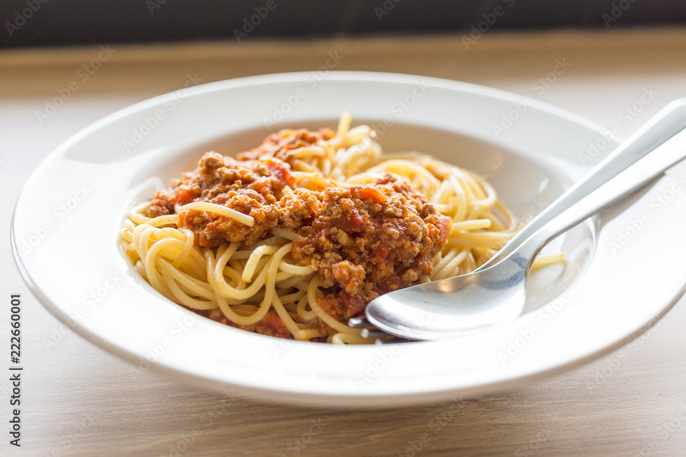 Cuisine and Food, Italian spaghetti pasta with meat and tomato sauce in a white plate on a wooden table.