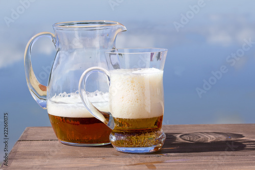 Pitcher with a mug of fresh beer on the table by the lake