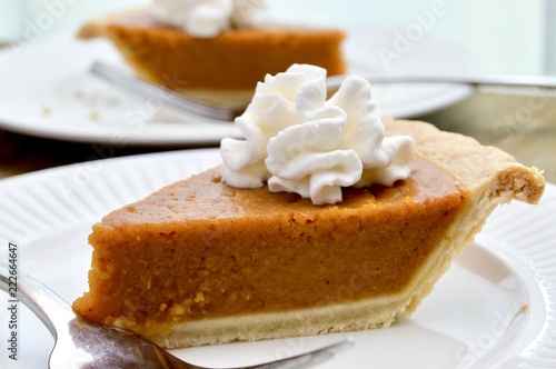 Slice of pumpkin pie with whipped cream on a white plate with fork