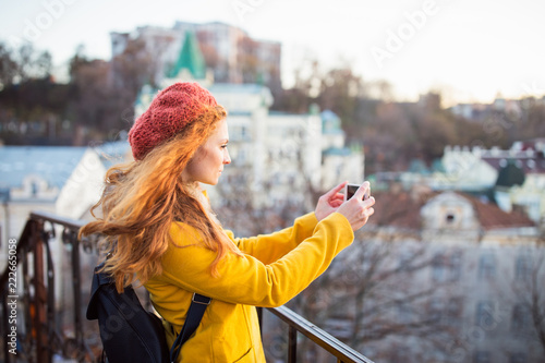 Red hair beautiful woman wearing yellow coat and orange beret with backpack walking outdoors. Autumn time, city on background