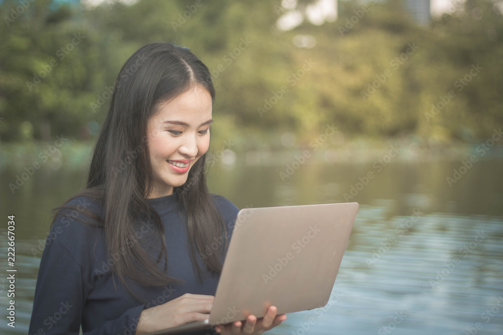 Young Asian woman using laptop on garden outdoor background.Happy freelancer working in the garden. Writing, surfing in the internet. Young Asian woman using laptop on garden outdoor background.Happy freelancer working in the garden. Writing, surfing in the internet.