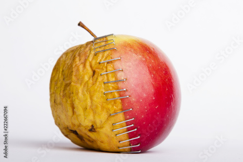 Fresh red and old yellow apple halves with staples on white background, plastic surgery  metaphor