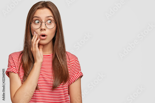 Concerned impressed shocked teenager looks with bugged eyes aside, keeps jaw ...