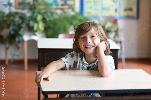 Petit garçon assit dans sa classe avec un grand sourire. La rentrée