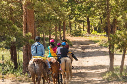 Family of four taking a horseback riding lesson in the woods in the Rocky Mountains, Colorado, in the summer photo