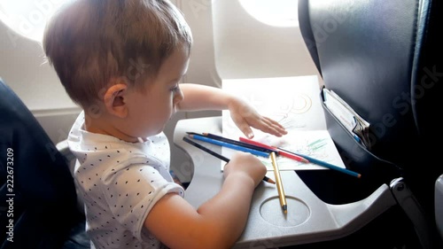 4k footage of little toddler boy drawing with colorful pencil on folding table at airplane during flight photo