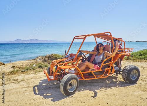 Tableau sur toile A happy girl driving a Buggy on a dune of beach with the Aegean sea in background