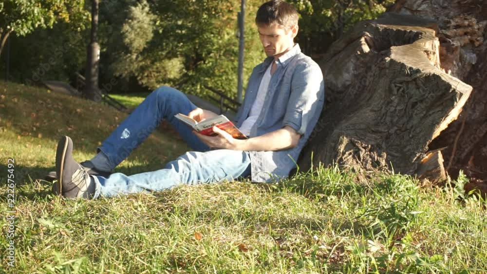 Man is reading book sitting on grass in park Man is reading book sitting on grass in park