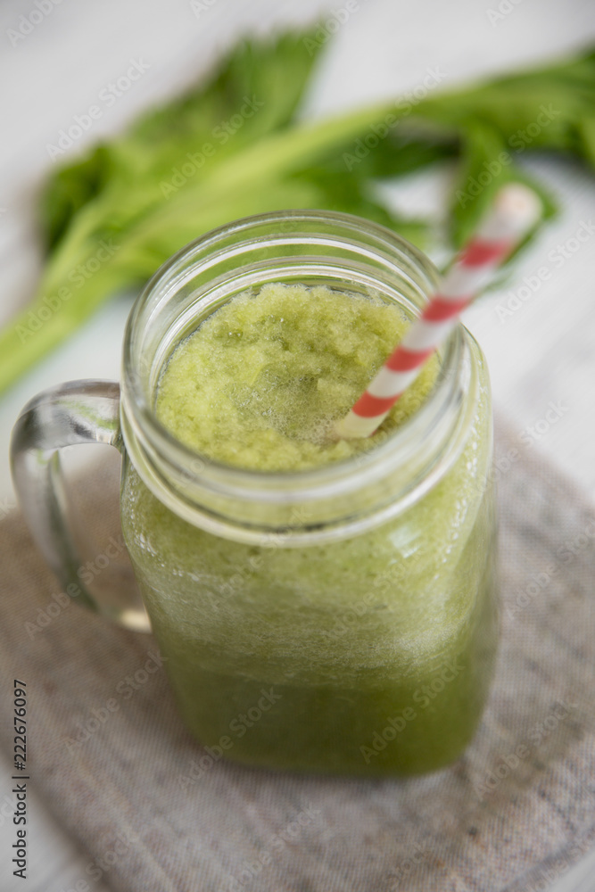 Glass jar of green celery smoothie on white wooden background, low angle view. Close-up. Glass jar of green celery smoothie on white wooden background, low angle view. Close-up.