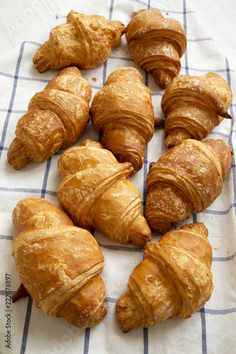 Fresh croissants on cloth on white wooden background, high angle view. Closeup.