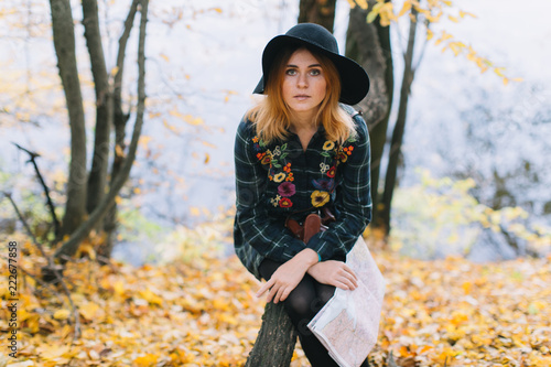 Hippie girl with a map, old camera in a hat walks autumn park.