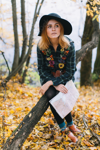 Hippie girl with a map, old camera in a hat walks autumn park.