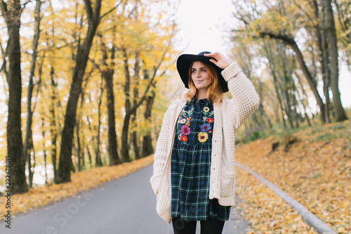 Stylish hippie girl in a knitted sweater and hat walks in the autumn park.