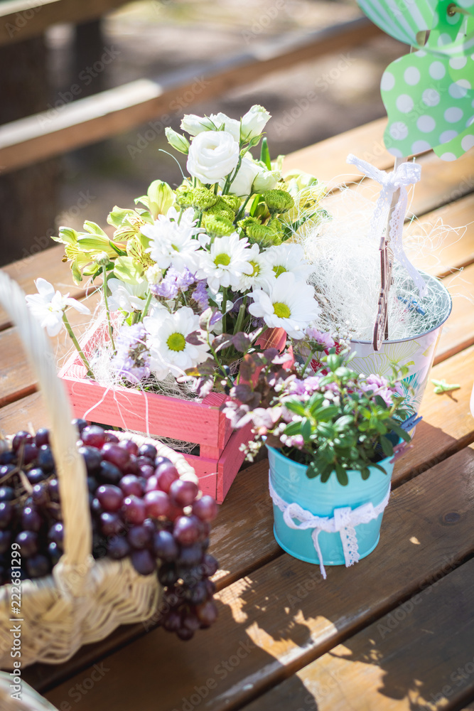 Picnic party table decoration: baskets with fruits on a wooden table, flowers, pink small guitar and pinwheel. Selective focus