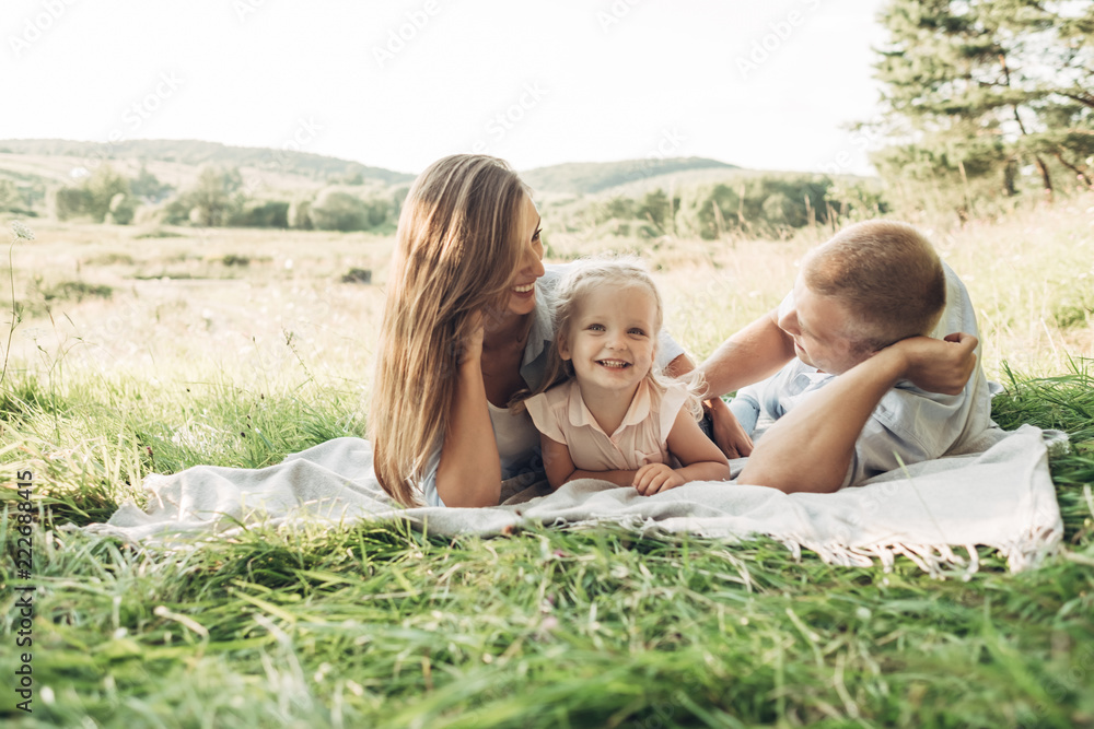 Young Adult Couple with Their Little Daughter Having Fun in the Park Outside the City, Family Weekend Picnic Concept, Three People Enjoying Summer Time
