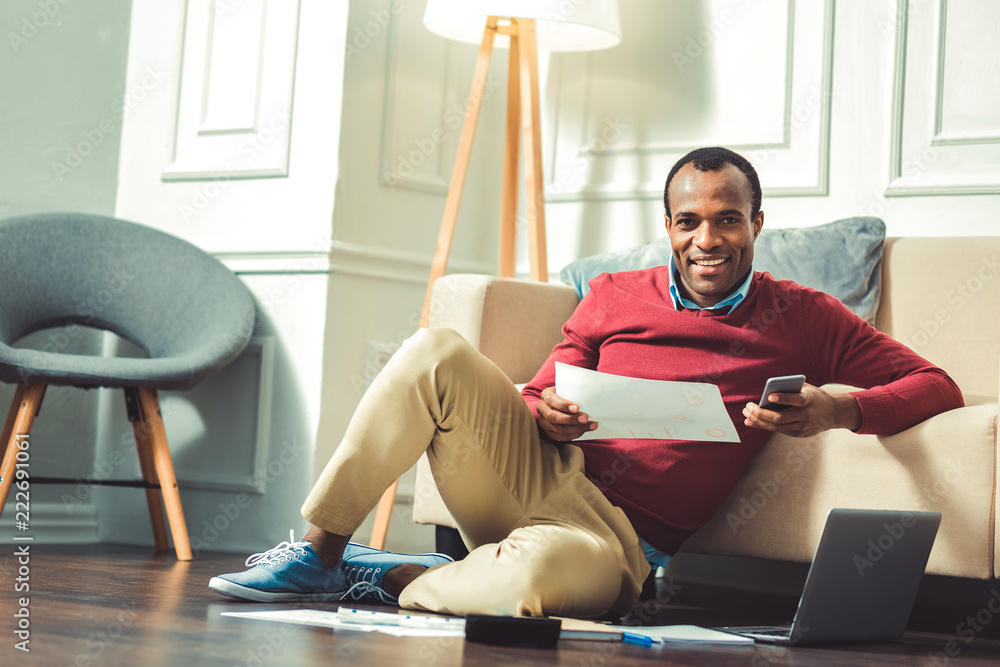 Useful app. Handsome afro american man seating on floor and looking at camera Useful app. Handsome afro american man seating on floor and looking at camera