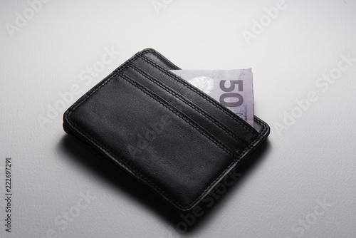 A black leather wallet on a white background with the corner of a NZ$50 note sticking out of the top.