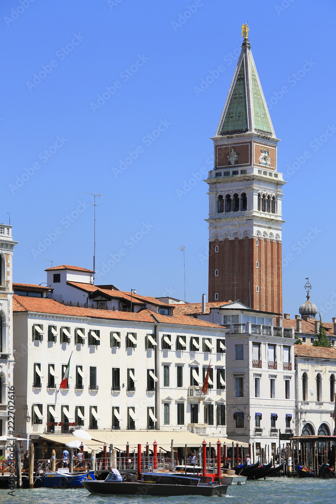 Fototapeta premium Venice canal, boat traffic, mooring posts and St Mark's Campanile, bell tower, in the background - famous place, Veneto, Italy; attraction, sightseeing, vacations, travel, romance, tourism.