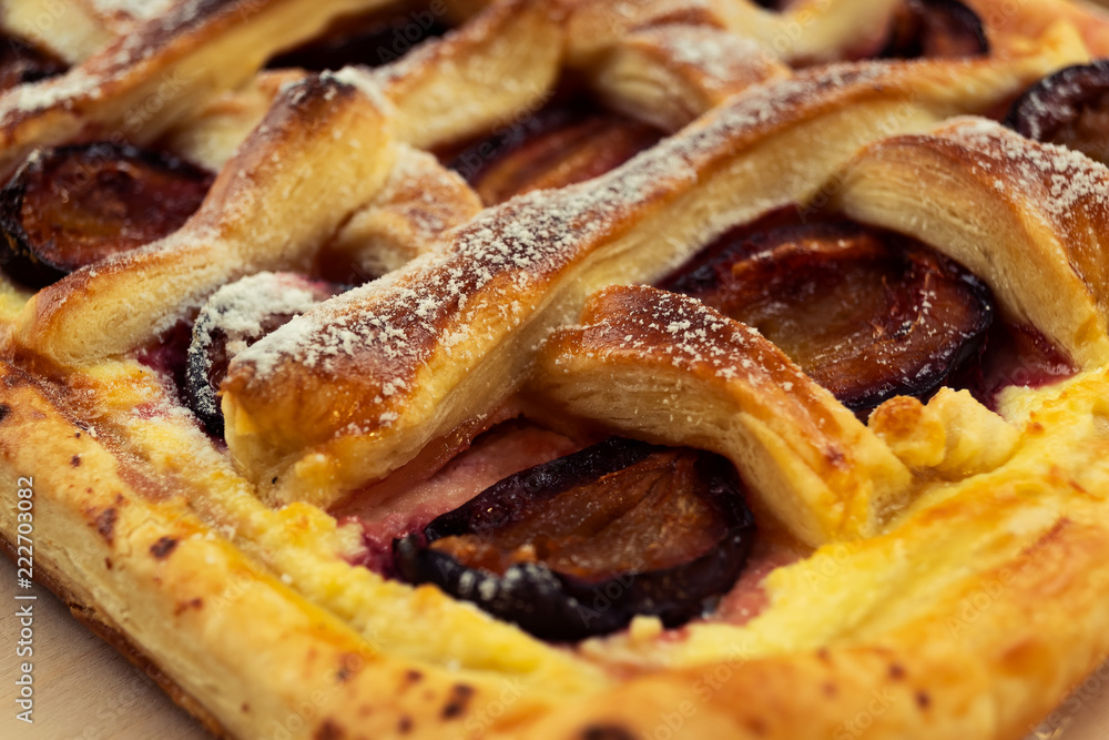 Puff pastry cake baked in the oven with plums, with powdered sugar, close-up.