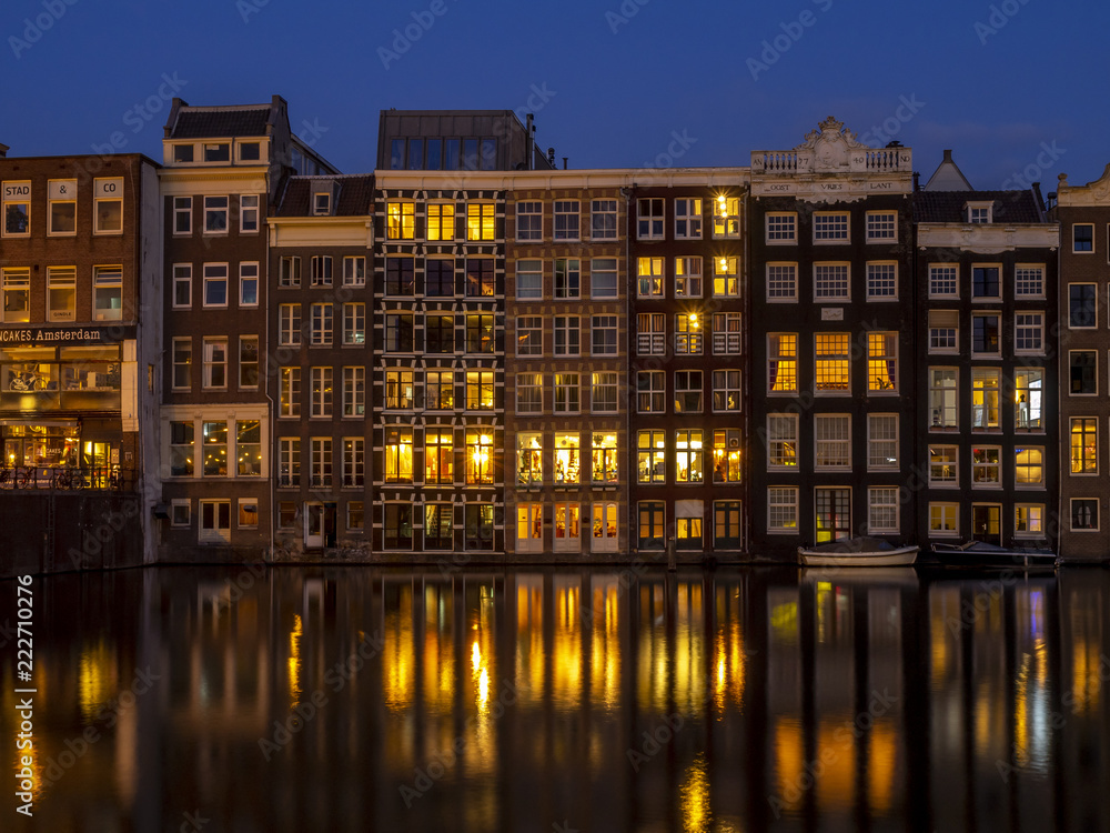 Traditional canal houses on the Damrak at dusk in Amsterdam. Buildings on the canal are a form of traditional Dutch architecture which is now very popular.