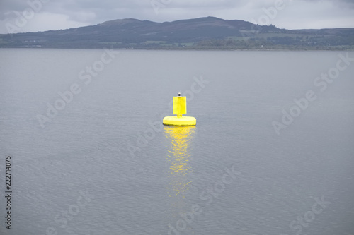 Yellow buoy bright light in open sea under dark grey clouds and mountain