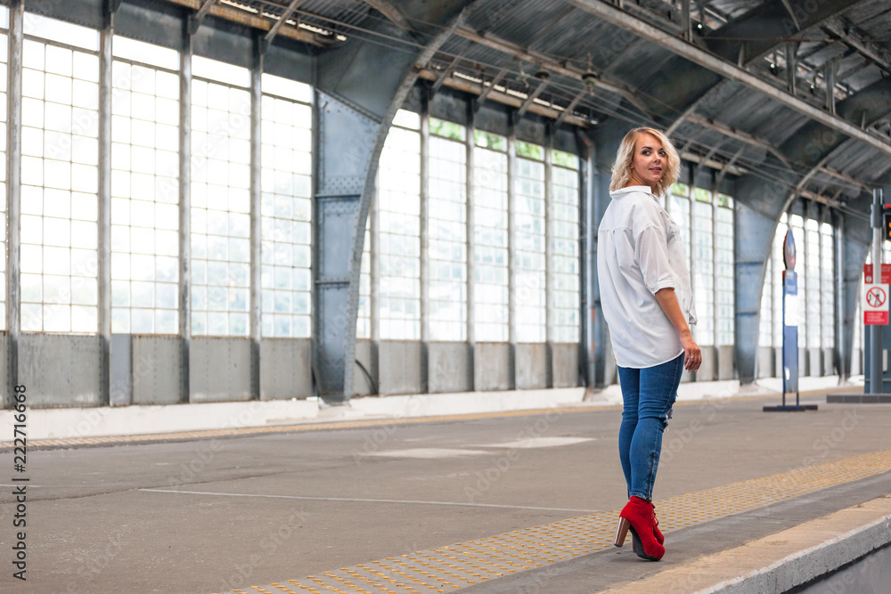young beautiful girl in a white shirt, blue jeans and red shoes goes on the platform at the old railway station young beautiful girl in a white shirt, blue jeans and red shoes goes on the platform at the old railway station