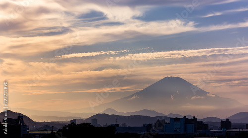 Mount Fuji surrounded by misty clouds before sunset, looming over a small city
